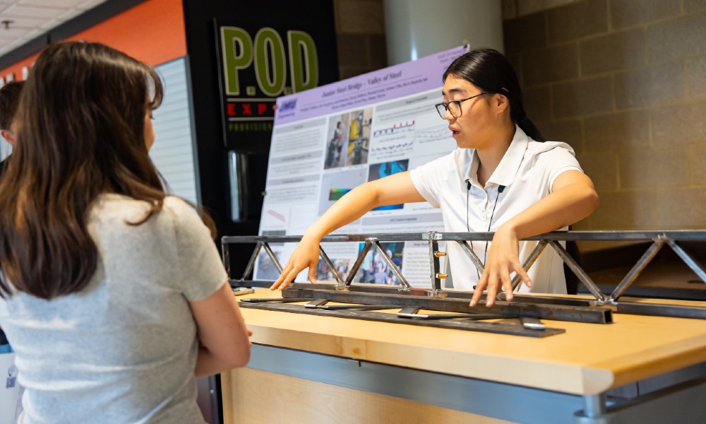 A student explains a steel-bridge model to a visitor at the CISE Student Showcase